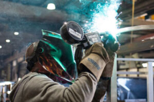 A welder at Mainland Machinery welds a metal structure slightly above his head.